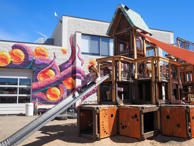 Junkyard's outdoor play structure with a little girl on the slide